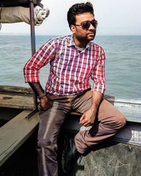Young man wearing sunglasses sitting on boat against sea