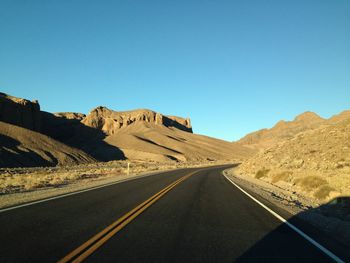 Road leading towards rocky mountains against clear blue sky