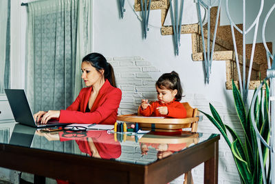 Young executive woman working from home while taking care of her young daughter