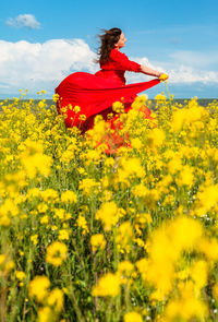 Rear view of woman standing amidst yellow flowering plants on field