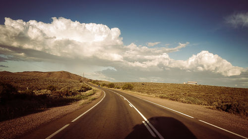 Empty road amidst landscape against cloudy sky