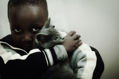 Portrait of boy embracing cat while sitting against wall