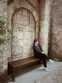 Side view of young woman sitting on old building