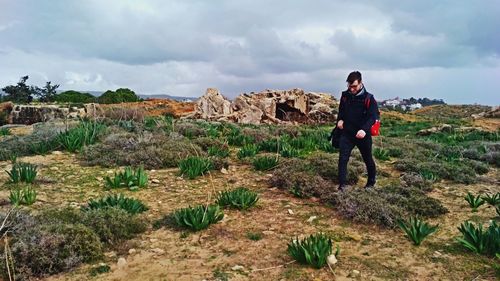 Full length of man walking on landscape against cloudy sky