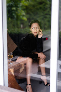 Portrait young woman sitting on armchair holding glass of wine in her hand shot through the glass
