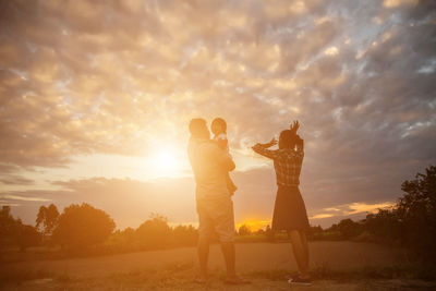 Friends standing on field against sky during sunset