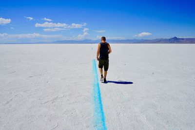 Rear view of man walking on salt flat against blue sky