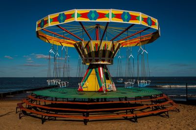 Ferris wheel on beach against blue sky