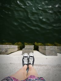 Low section of woman standing on retaining wall by lake