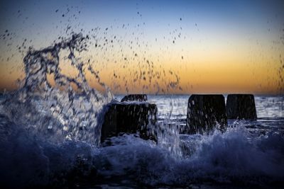 Water splashing in sea against sky during sunset