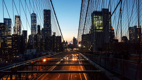 Illuminated bridge and buildings against sky at dusk