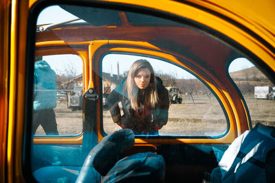 Smiling young woman sitting by yellow car
