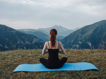 Rear view of woman sitting on mountain against sky