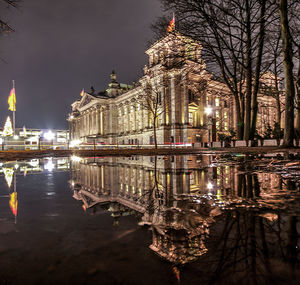 Illuminated reichstag building by lake against sky at night