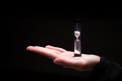 Close-up of hand holding hourglass against black background