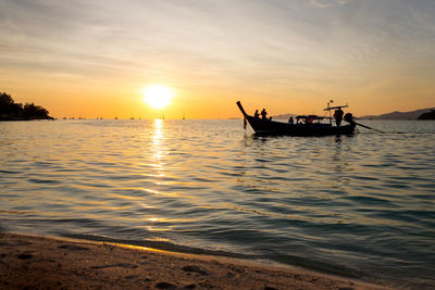 Silhouette people on longtail boat in sea during sunset