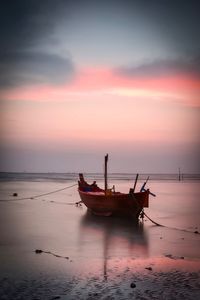 Boat moored in sea against sky during sunset