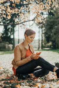 Young woman using smart phone while sitting on sidewalk