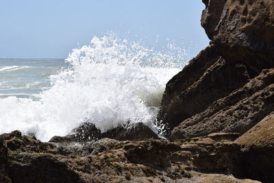 Waves splashing on shore against clear sky