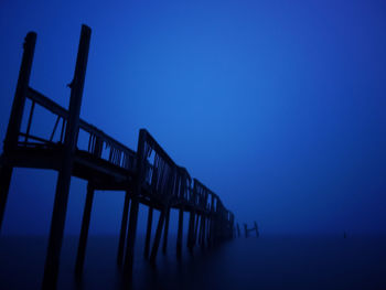 Pier over sea against clear blue sky at dusk