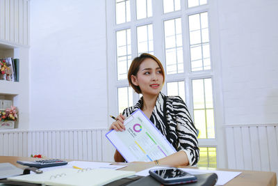 Portrait of young woman standing against window