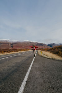 Woman in a red jumper and a scarf running on the road in iceland with arms spread