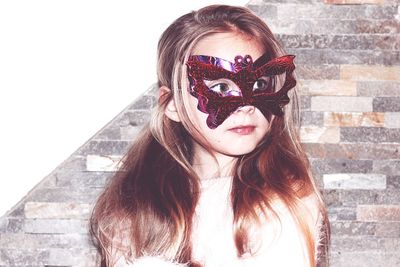 Girl wearing masquerade mask against wall