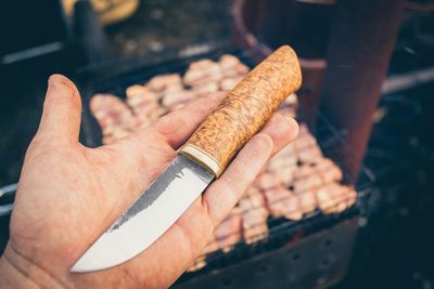 Cropped image of person holding meat on barbecue grill