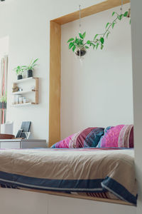 Light modern minimalist bedroom interrior with bed, pillows, shelves, and hanging green plants.