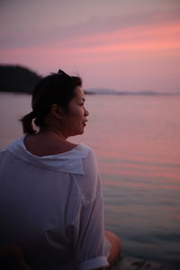 Rear view of woman sitting at beach during sunset