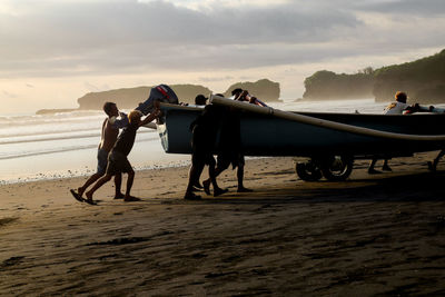 People on beach against sky during sunset
