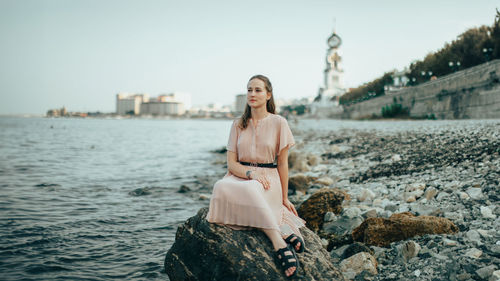 Portrait of young woman sitting on rock by lake