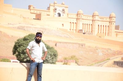 Portrait of young man with hand on hip standing against fort