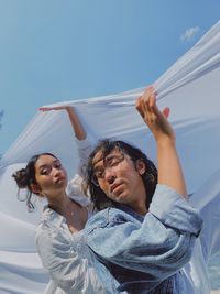 Low angle view of man and woman holding textile against sky