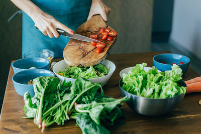 An unrecognizable female hands prepares a salad and puts the ingredients in a large bowl. 