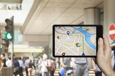 Cropped hand of person holding digital tablet with map in city