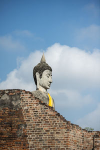 Low angle view of buddha statue by old brick wall at wat yai chai mongkhon