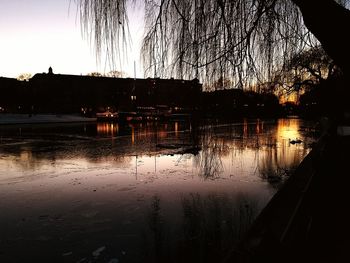 Reflection of silhouette trees on wet water against sky