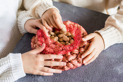 Children's hands reach unpeeled peanuts from a mesh bag on the table. 