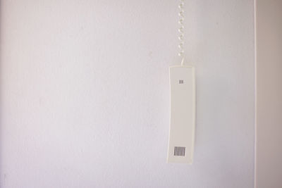 Close-up of telephone receiver hanging against white wall