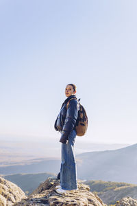 Female hiker with backpack standing on top of mountain against clear sky