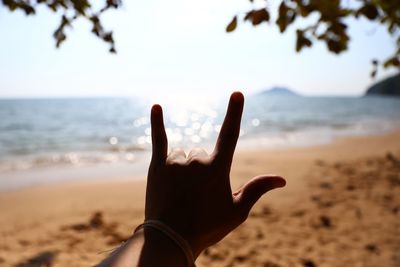Cropped hand showing rock sign at beach