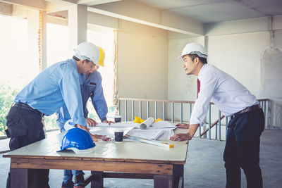 Young engineers leaning on table with blueprints at construction site