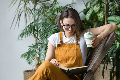 Smiling woman reading book and having coffee while sitting on chair