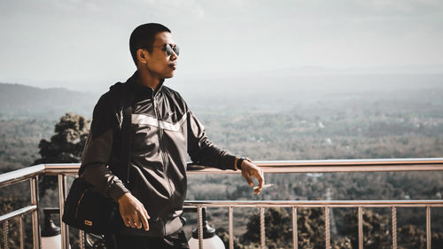 Young man looking away while standing on railing