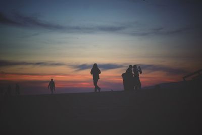 Silhouette people standing on beach against sky during sunset