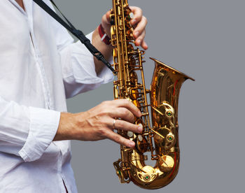 Midsection of man playing saxophone against gray background