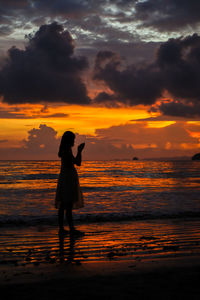 Silhouette boy standing on beach against sky during sunset