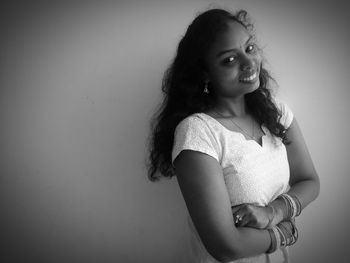 Portrait of cheerful young woman with arms crossed standing against wall