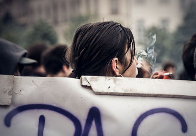 Woman smoking cigarette while standing by poster in city